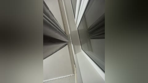 Video of a modern ceiling corner with clean, minimalist lines. The corner features a white ceiling with a grey border, and a grey curtain partially covering a window, creating a geometric, symmetrical pattern. The lighting is soft and diffused, emphasizing the architectural details.