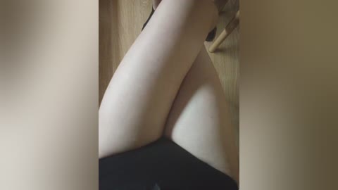 Media: A close-up video of a person's legs in black stockings, with light skin, sitting on a wooden floor, blurred background.