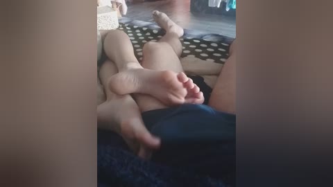 Video of a young girl with light skin, lying on a dark carpeted floor, wearing a black dress, with her feet playfully resting on another person's bare feet.