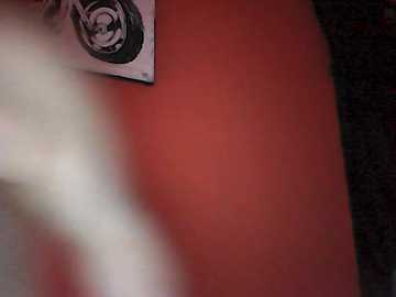 Video of a person's blurred lower half standing against a vibrant orange wall, with a black-and-white sketch of a face on the left. The background is dark with a textured fabric.