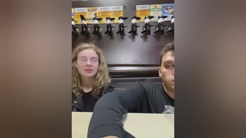 Media: A video of two people, a woman with curly blonde hair and a man with short brown hair, sitting in a fast-food restaurant. The background shows a shelf with toy penguins and a menu board.