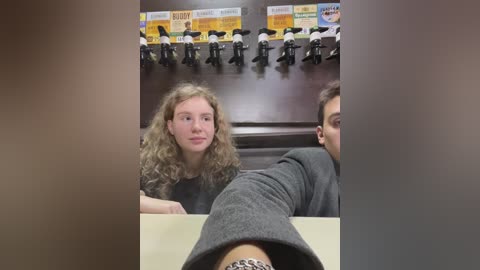 Media: Video of three people, including a woman with curly hair and a man with short hair, sitting at a table in a restaurant. Background includes a wall with toy figurines and a menu.