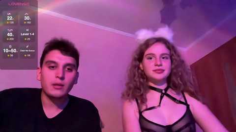 Media: Video of a young man with short dark hair in a black shirt and a young woman with curly hair, wearing a black strappy lingerie top, in a dimly lit room with purple lighting and a \"Live Stream\" overlay.