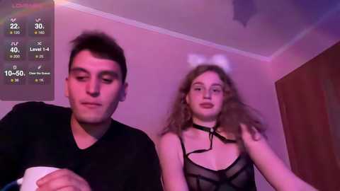Media: Video of a man and woman, both wearing black outfits, in a dimly lit room. The woman has curly hair and a white headband, and the man has short hair.