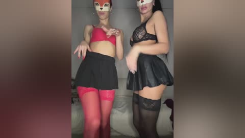 Video of two women in provocative red and black lingerie, fox face masks, and thigh-high stockings, standing side-by-side indoors.