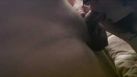Video of a man in a dimly lit room, partially clothed, holding a black object to his mouth, possibly a cigarette.