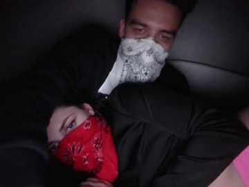 Video of a man with a white surgical mask and a red bandana covering his mouth, lying next to a woman in a black jacket, both in a dark, confined space.