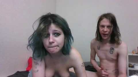 Media: Video of two nude, thin people with blue hair, in a dimly lit room. One is kneeling, the other standing.