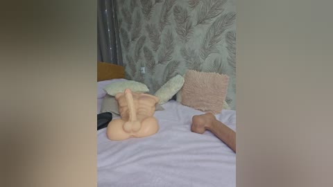 Media: A video of a bedroom with a beige cat toy on a white bed, two pillows, and a beige fluffy pillow, against a patterned green wall.