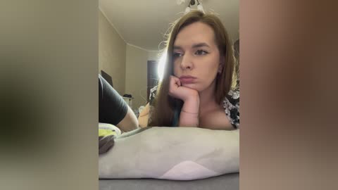 Media: A video of a young woman with long brown hair, lying on a bed, looking thoughtful, wearing a black and white patterned shirt, in a dimly lit room.