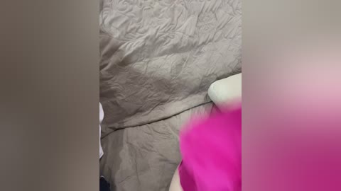 Media: A close-up video of a person's torso wearing a beige, wrinkled shirt and a bright pink bra visible through the shirt, with blurred faces on either side.