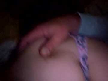 Video of a close-up, dimly lit scene featuring a light-skinned person's upper body, with a hand touching their breast. They are wearing a lavender bra with a floral pattern. The background is dark and indistinct.