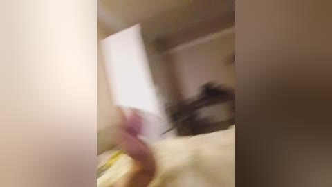 Blurred video of a person with a pink phone, possibly in a bedroom with beige walls, a bed, and a window. The image is out of focus, making details indistinct.