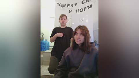 Media: Video of a young woman with shoulder-length brown hair in a salon chair, wearing a gray robe. Behind her, a young man in a black shirt and brown pants stands, looking concerned. The salon background includes a blue plastic bag and Russian text.