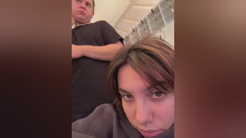 Media: A video shows a young woman with medium-length brown hair, looking up at a man wearing a black shirt in a bathroom with a tiled shower wall.