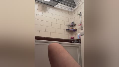 A video of a person's leg in a bathroom, featuring white subway tiles, a wooden countertop, and a shower caddy with toiletries.