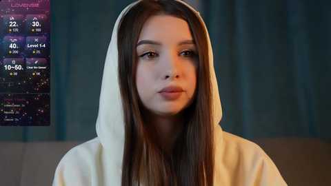 Media: Video of a young woman with long brown hair, wearing a white hooded robe, in a dimly lit room with a digital clock displaying 12:30 a.m.