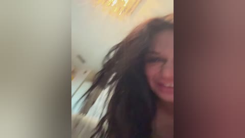 Media: A blurry video of a woman with long, dark hair, smiling, partially visible face, and a golden chandelier in the background.