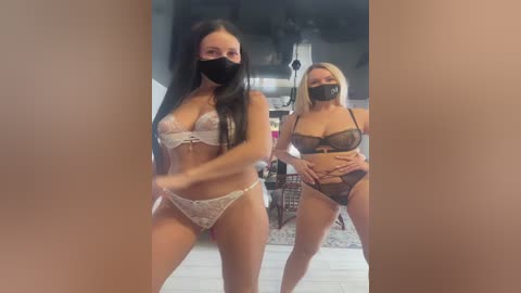 Media: Video of two women in lingerie, one with long black hair and light skin, the other with short blonde hair and fair skin, both wearing black face masks, in a modern indoor setting.