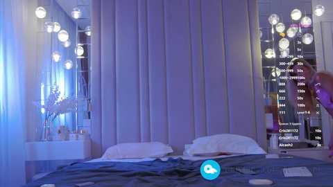 A video of a modern, dimly-lit bedroom with a plush, white bed, sheer curtains, and a mirrored wall displaying a city skyline.