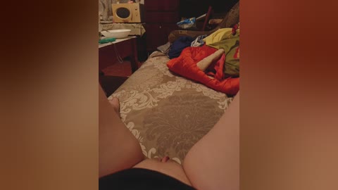 Video of a pregnant woman in a bedroom, lying on a bed with a floral-patterned sheet. She wears a red shirt and has a visible belly. Background includes a cluttered dresser and a stuffed animal.