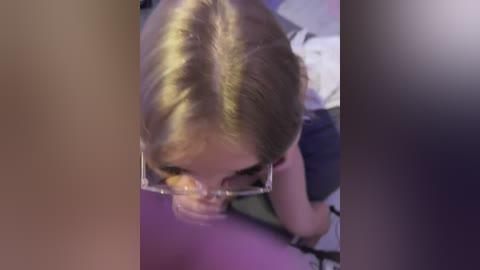 Media: A blurry video shows a young woman with light skin and blonde hair, wearing glasses, bent over, possibly performing oral sex on a man. The background is indistinct and dark.