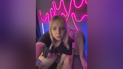 Video of a young woman with platinum blonde hair, wearing a black t-shirt, sitting in front of a neon \"Wu-Tang Clan\" sign.