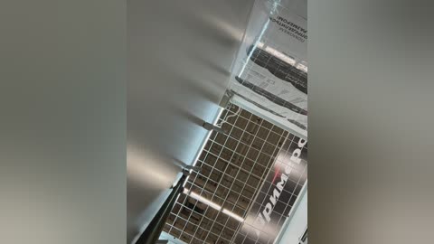 A video of a modern office ceiling with metal grid panels, fluorescent lighting, and a blurred, reflective surface. The image is taken from a low angle, emphasizing the grid pattern and light reflections.