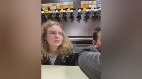 Media: A video shows a blonde woman with curly hair and a gray shirt, seated in a restaurant booth with a view of a row of black and white motorcycle figurines.