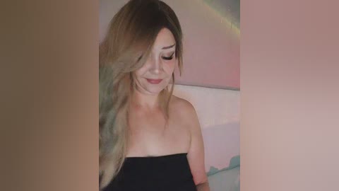 Video of a smiling woman with long, wavy, multi-colored hair, wearing a strapless black dress, set against a blurred, pink and green background.