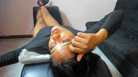 Video of a Black woman lying on a massage table, wearing a black long-sleeved top and black shorts, with a masseuse's hand on her face.