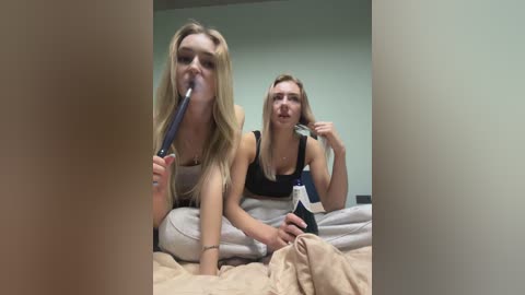 Media: A video shows two young women with long blonde hair, wearing black tank tops, lying on a bed. One brushes her teeth with a blue toothbrush; the other holds a phone, smiling.