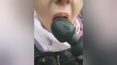 Video of a light-skinned child with fair hair, wearing a white shirt and black jacket, sucking on a black object, likely a pacifier, while seated in a car.