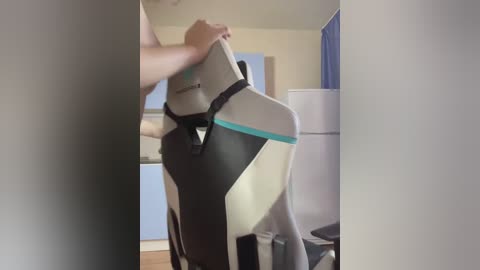 Video of a person wearing a black and gray exercise mat with turquoise accents, standing in a modern, minimalist kitchen with light-colored cabinets and a white refrigerator.