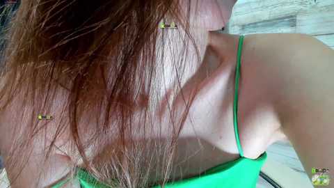 Video of a woman with fair skin and long brown hair, wearing a green spaghetti strap top, seen from behind, showing her neck and upper back. The background is a tiled floor with a light color palette.