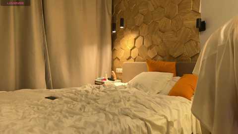 Media: Video of a cozy bedroom with a wooden-textured headboard, beige bedding, orange pillows, and a bedside table with a small lamp. Warm lighting enhances the rustic, modern ambiance.