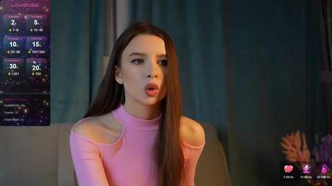 Media: Video of a young woman with long brown hair, wearing a pink off-shoulder top, with a surprised expression, in a dimly lit room.