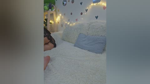 Video of a woman lying on a white, fluffy rug in a cozy room with a wooden bookshelf, heart decals, and string lights in the background.