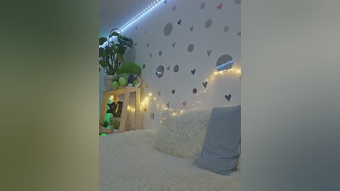 Video of a cozy, whimsical bedroom with white walls adorned with heart-shaped decals, a plush white bed, and a wooden bedside table holding potted plants. Soft, warm fairy lights and a blue throw pillow add a calming, inviting atmosphere.