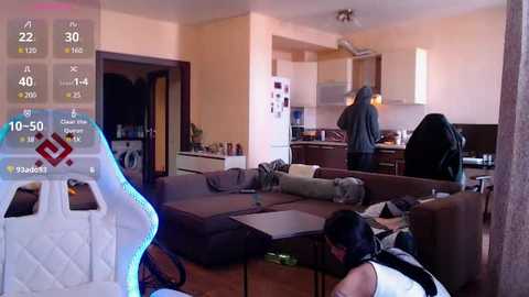 Video of a modern living room with a gaming setup, featuring a large TV, gaming chair, and controller, with a person seated in the background.