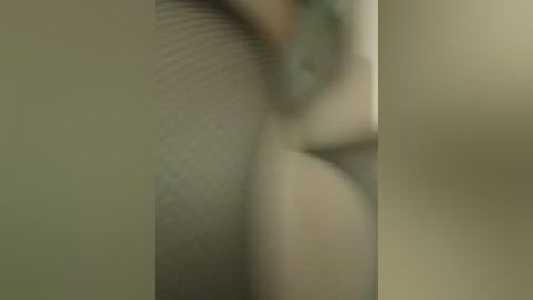 Blurry video of a person's upper torso and arm, likely female, with fair skin, partially obscured by a soft, beige background.