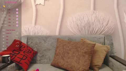 Video of a cozy living room with a light blue velvet sofa, adorned with patterned red pillows, beige and gold throw pillows, and a white decorative branch wall hanging.