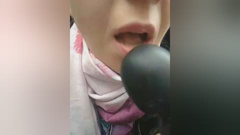 Video of a close-up of a person with fair skin, wearing a pink and white patterned scarf, singing into a black microphone, with their mouth open.