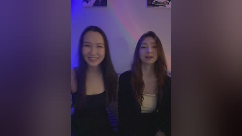 Media: Video of two young women with long hair, smiling, in a dimly lit room, one wearing a black top, the other a beige top, with a purple and blue light effect on the background.