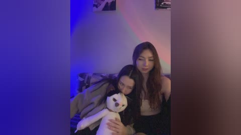 Media: Video of a young woman with long hair, wearing a black sweater, holding a small white dog, sitting on a couch, with a blue and purple light effect on the wall.