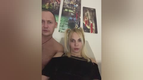 Media: Video of a topless, muscular man with short hair and a tattooed neck standing behind a blonde woman with pigtails, wearing a black dress, in a room with Venetian canal paintings on the wall.