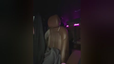 Media: Video of a dimly lit car interior, showing a tan leather seat with ribbed detailing and a gray blanket draped over it. Purple neon lights illuminate the background, creating a moody atmosphere.