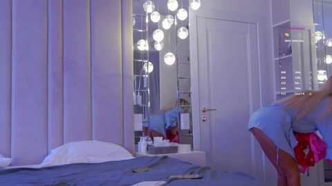 Video of a modern, minimalist bedroom with a white bed, large mirror, and hanging spherical pendant lights. The room exudes a serene, clean aesthetic with soft purple and white tones.