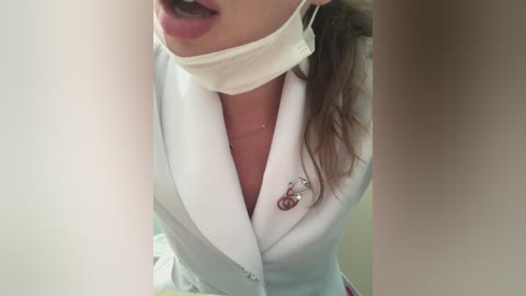 Media: Video of a woman in a white lab coat with a stethoscope, wearing a white mask, her mouth slightly open, and brown hair tied back.