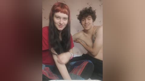 Media: A video of a pale-skinned woman with red hair and a man with curly dark hair, both shirtless, sitting on a bed in a room with floral wallpaper.